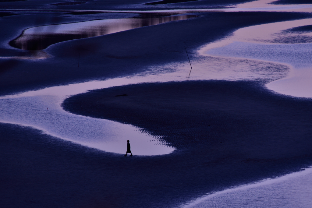 夕日が沈んだ後の干潟を歩く女性。