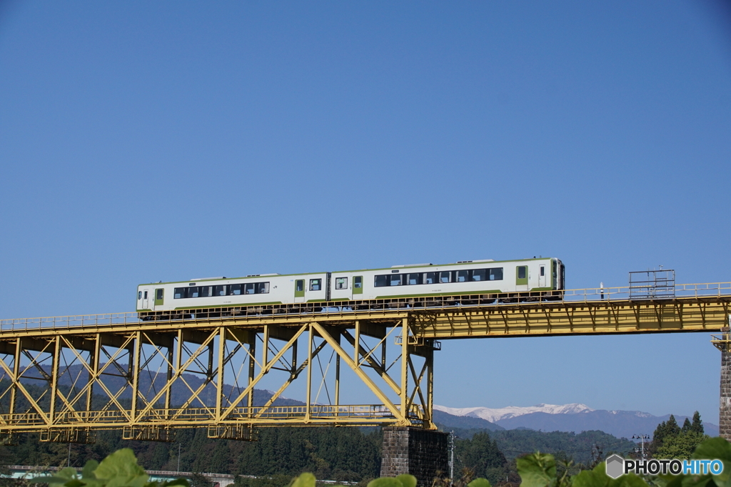 青空と黄色い鉄橋に白い列車と冠雪の飯豊連峰！