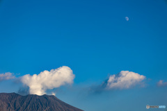 月のある青空に白雲の噴煙あげる桜島山