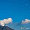 月のある青空に白雲の噴煙あげる桜島山