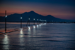 海に灯る海床路の明かりと雲仙普賢岳のシルエット