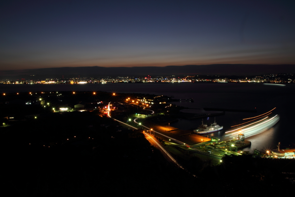 夜の光に包まれる桜島港と向こうの鹿児島市