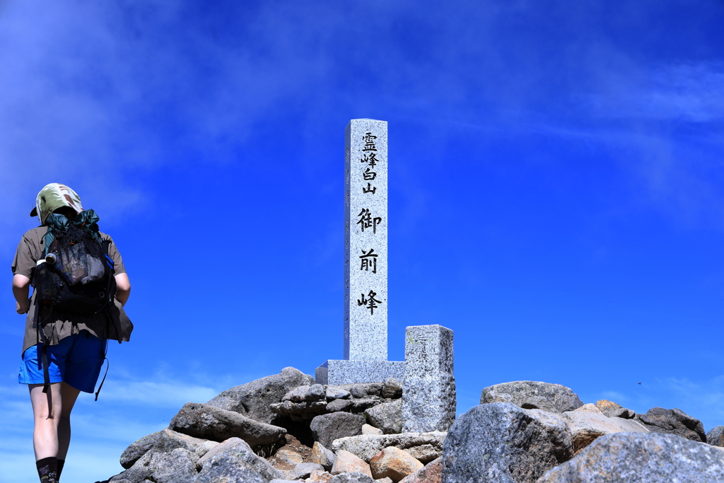 山頂の三角点を通過する登山者