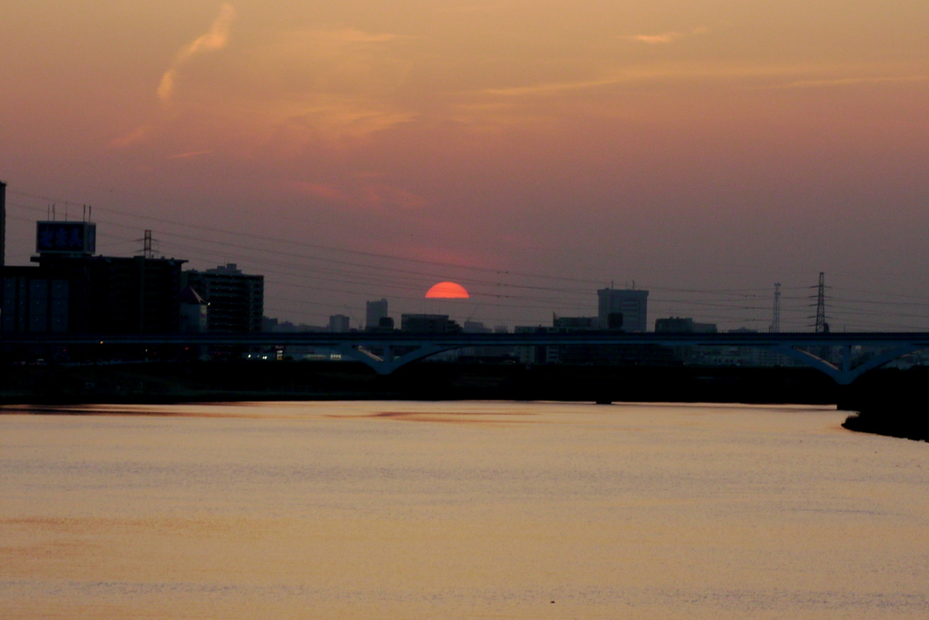 遠くの武蔵高丸の半分沈む春霞の夕日の見える荒川