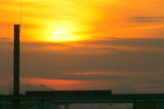 隅田川の煙突の下に走る舎人ライナーの上の雲被る夕日