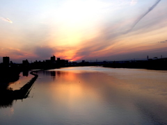 遠くの夕日のほうへ黒いジェット雲の荒川