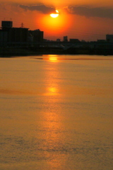 丸いベールの夕日に黒雲が掛かった荒川のサンロード