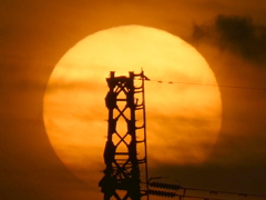 鉄塔の後ろの雲被る大きな夕日