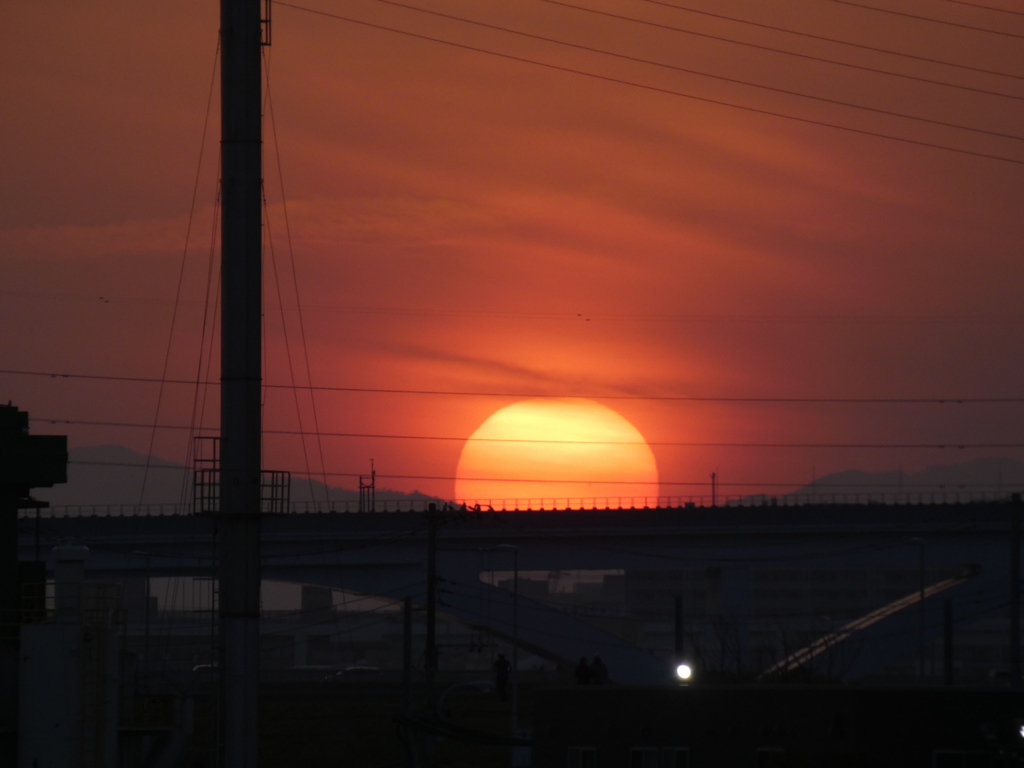 隅田川の煙突の後ろの舎人ライナーの高架上蕨山と大持山との谷の夕日