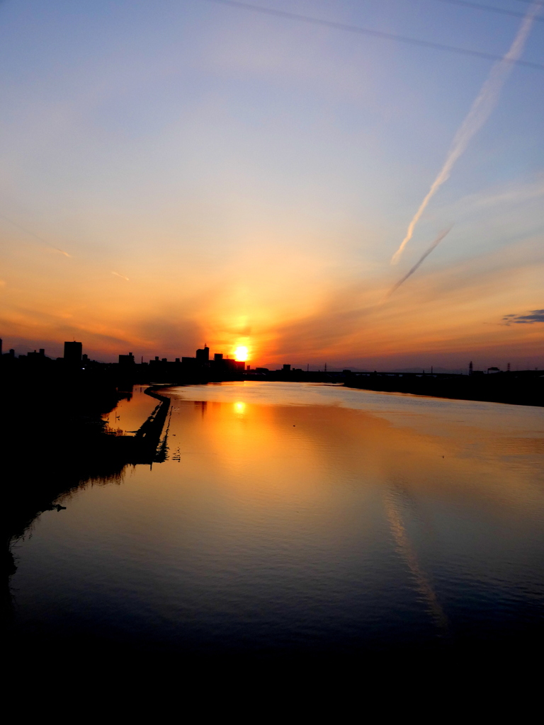 ジェット雲が荒川川面に映るおおきなアークの夕日