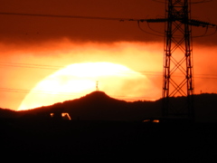 千住新橋から高速道路上の鉄塔の左の赤久縄山頂の大きな夕日