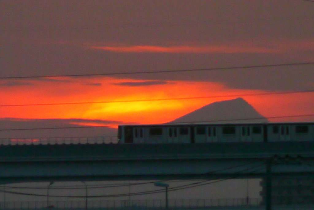 武甲山の夕焼けの前を舎人ライナーが