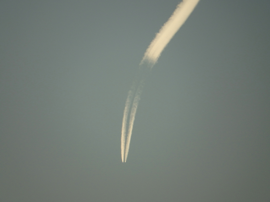 夕日を浴びるカーブした遠い飛行機雲