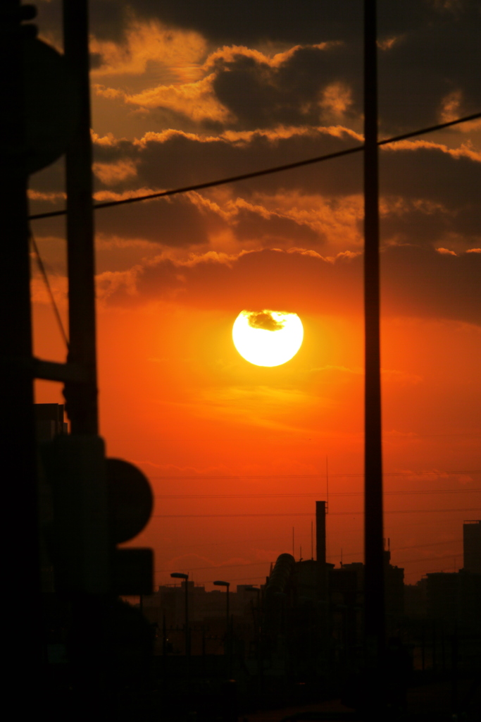 鉄塔と街灯のポールの間の夕日