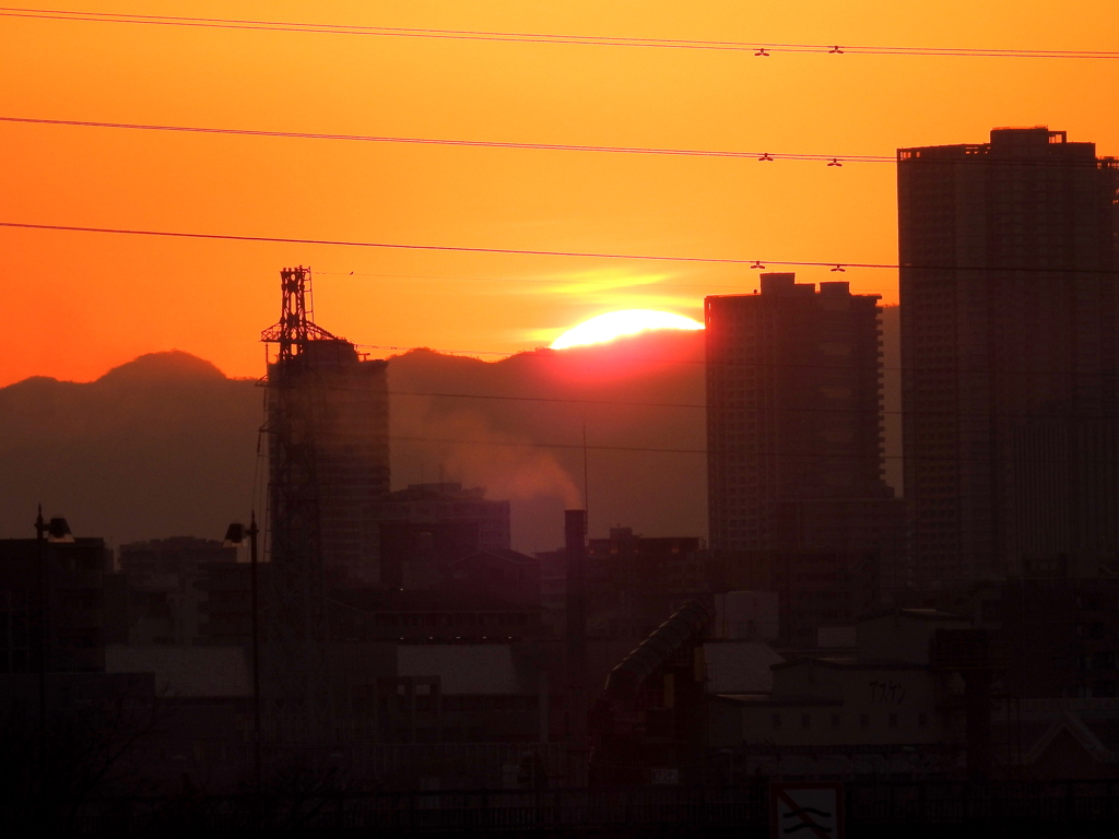 少し黄金色の雲を被る夕日が丹沢山系の山に
