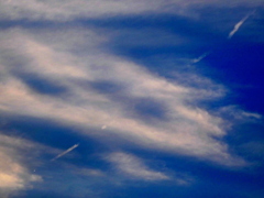 夕方の薄い彩雲の中の飛行機雲