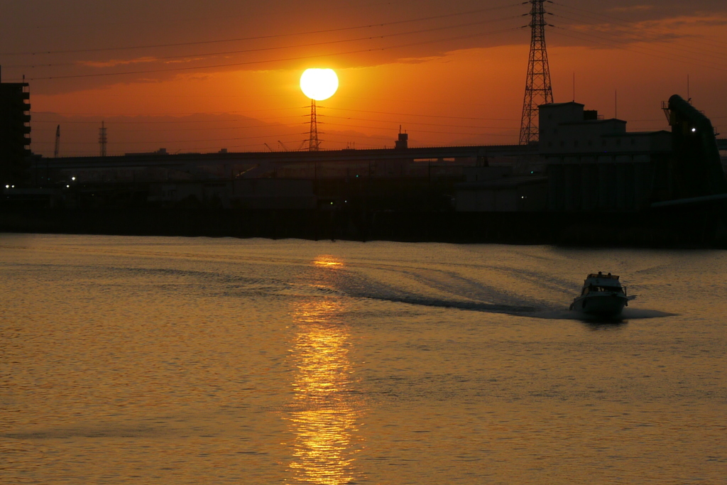 隅田川の夕日とこちら下流に向かう波しぶきの小型クルーザー
