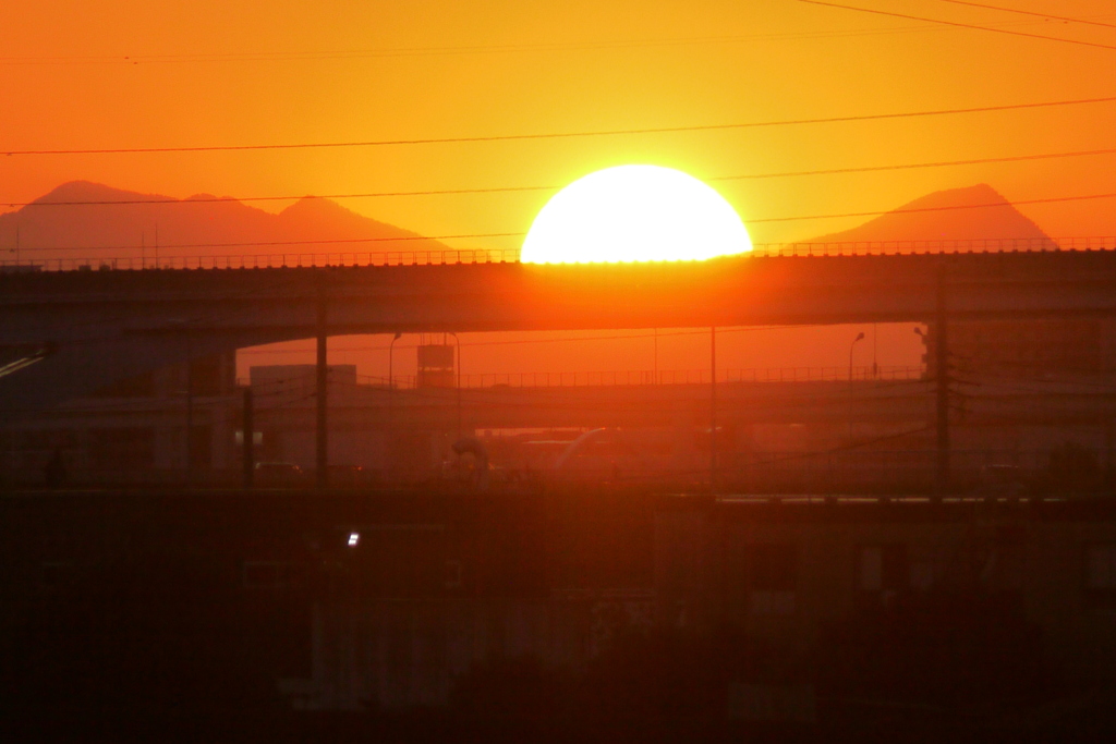 舎人ライナー高架の上の左大持山小持山と右武甲山の間に落ちる夕日