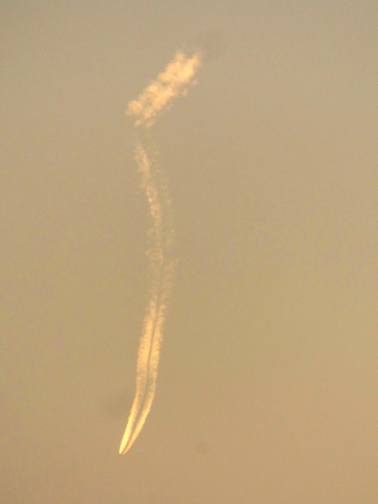 かなり遠い上から下へ向かうように見える夕日を受ける飛行機雲