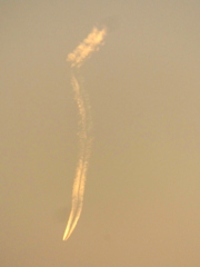 かなり遠い上から下へ向かうように見える夕日を受ける飛行機雲