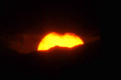 暮れの丹沢山系と大きな雲の間をを沈みながら右にすべる夕日