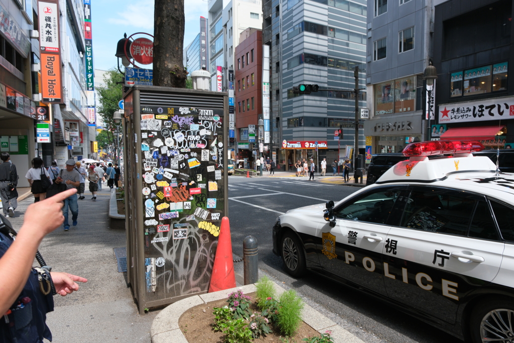 渋谷の電話ボックスとパトカーと警察官の腕