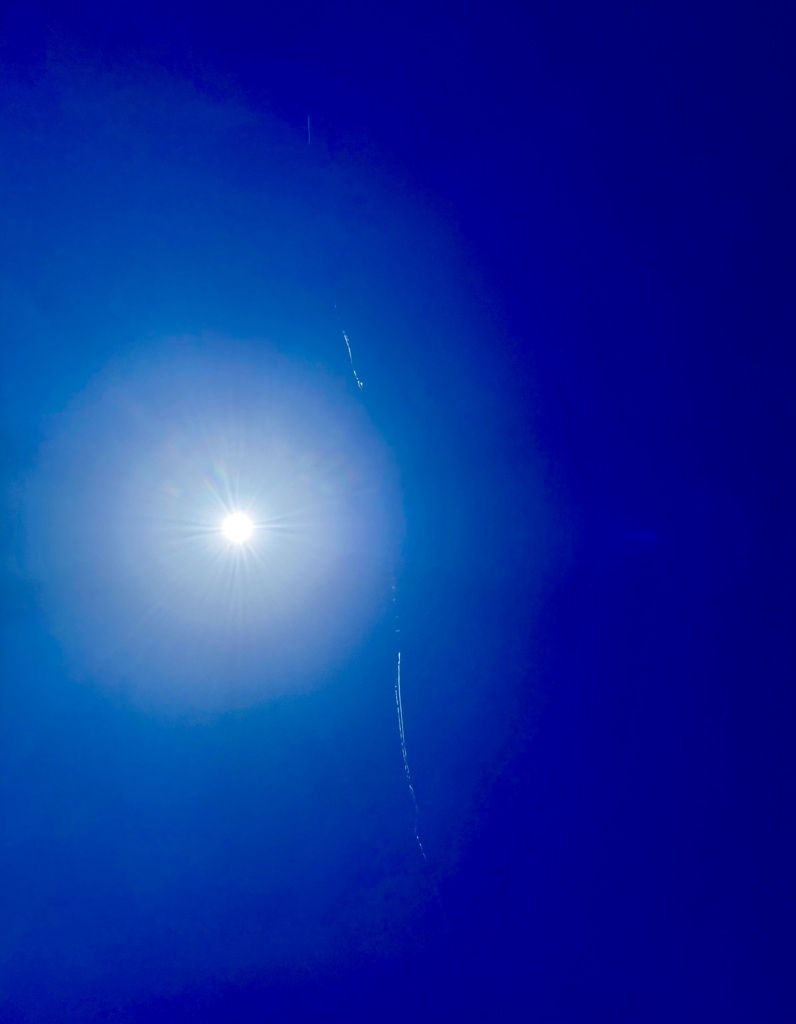 眩しい太陽によろける飛行機雲