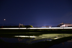 田園を横切る光の帯と三日月