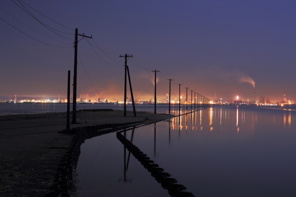 海に向かって伸びる電柱と工場の灯りが見える風景