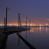 海に向かって伸びる電柱と工場の灯りが見える風景