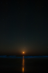 沈む月に夜光虫の波と星空。