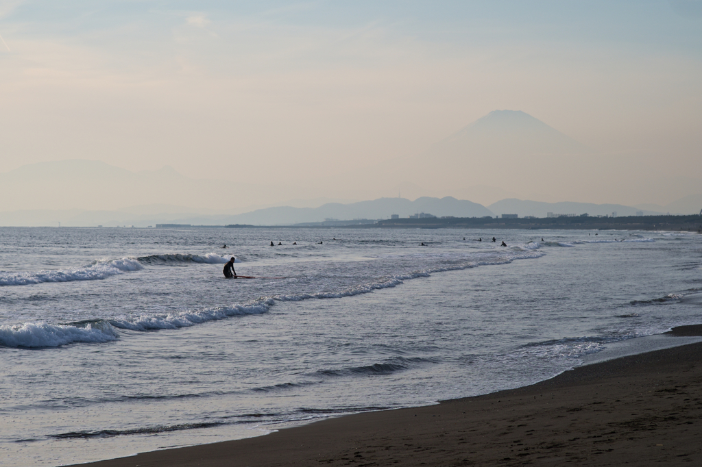 霞む富士と波に興じる人々