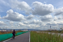 雲と河川敷と自転車の人