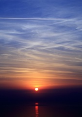海に映る夕日と飛行機雲 