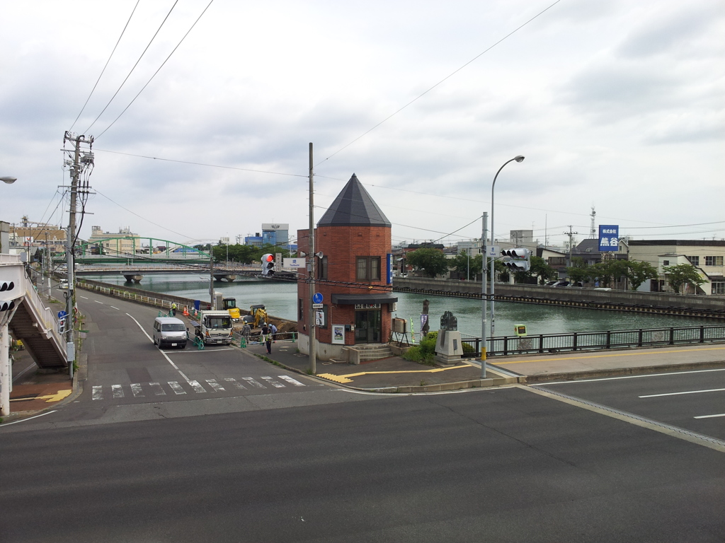 2018/07/16_堤交差点歩道橋から堤町交番と堤川を望む