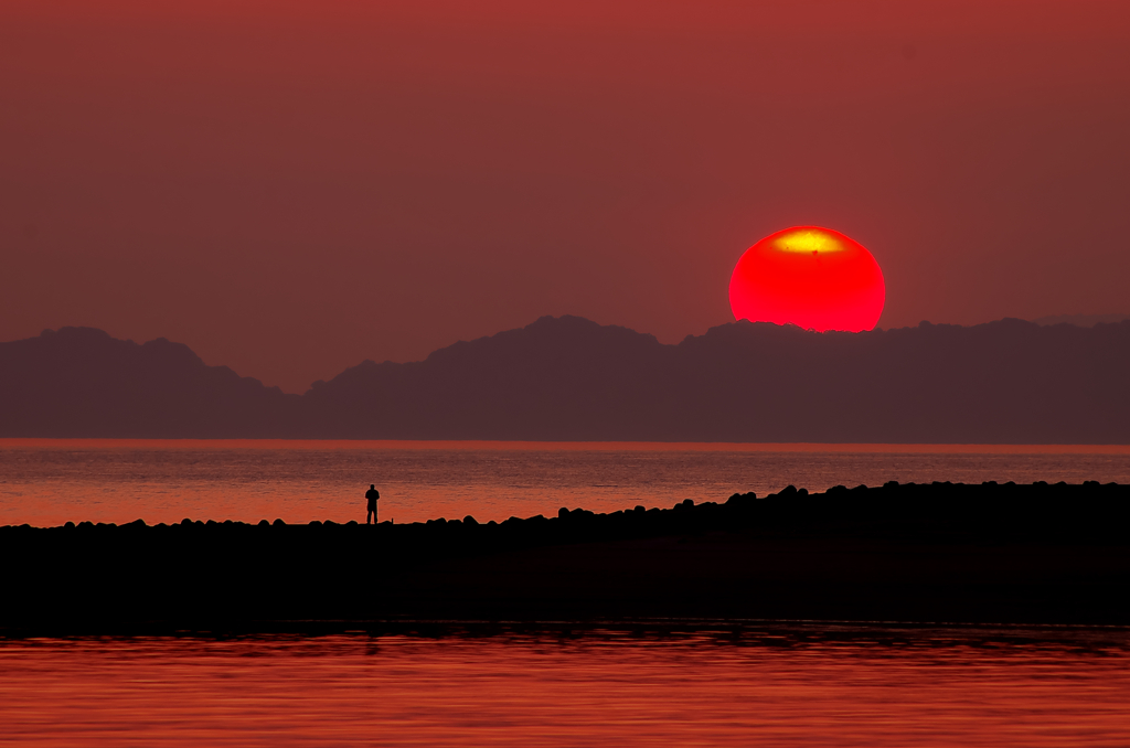 中島に落ちる夕日と釣り人