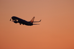 オレンジの空をバックに飛ぶJAL機
