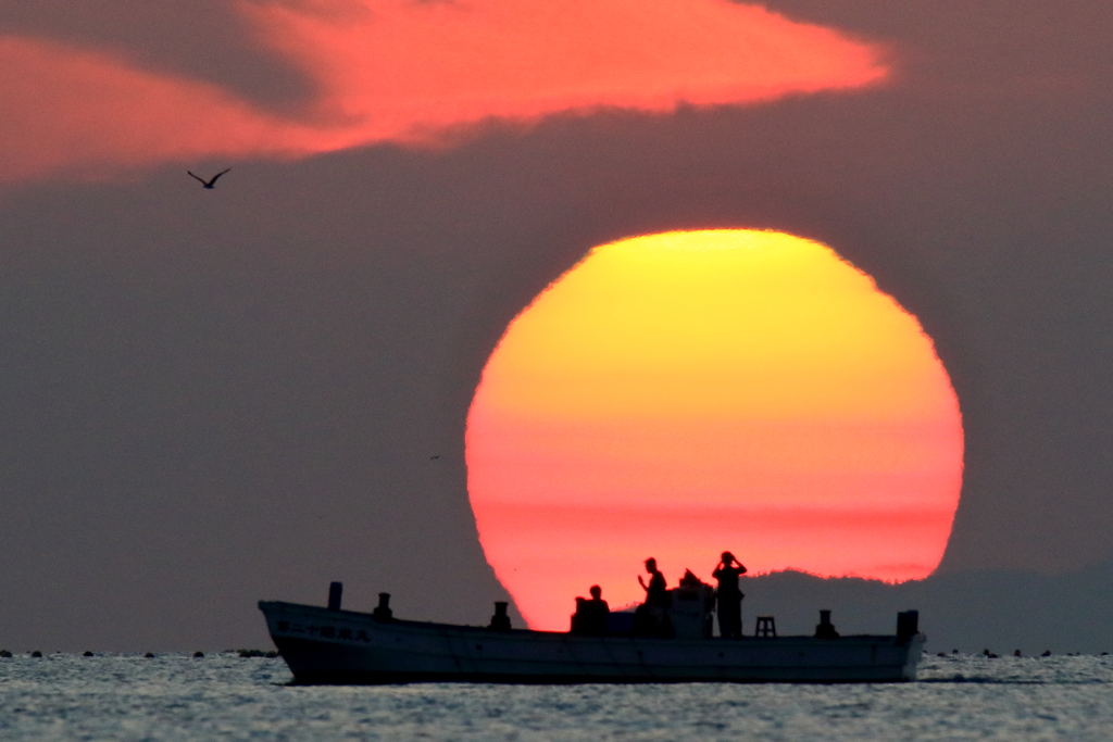 富山湾の端から登る朝日を横切る漁船に乗っている漁師さんと同じ朝日を見ている