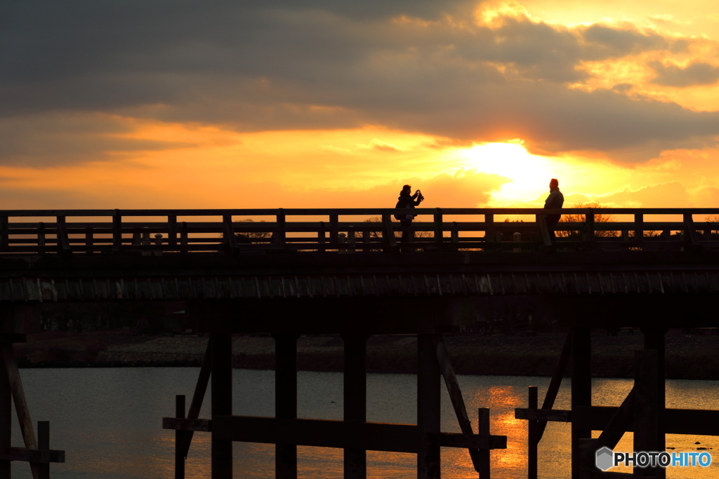 朝陽を浴びる渡月橋で写真を撮る人