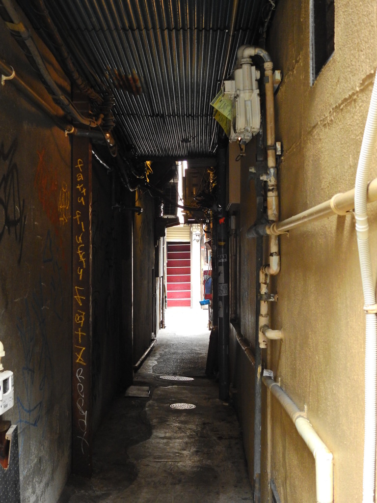 トタン屋根の路地裏の向こうの赤い階段